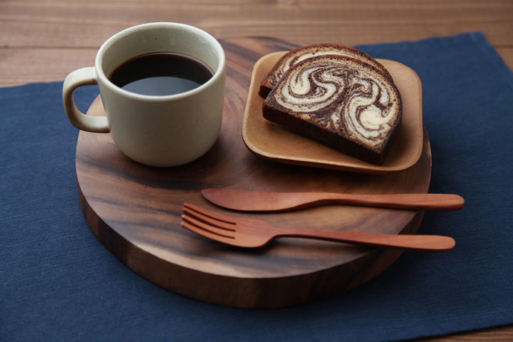 Acacia plate, utensils, and coffee cup next to a slice of bread