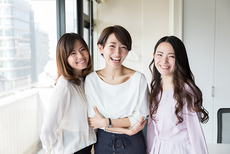 Three professional women standing in an office and smiling at the camera